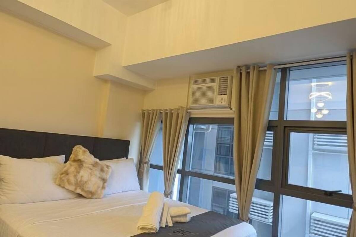 A hotel room with a bed, curtains, an air conditioning unit, and a window.