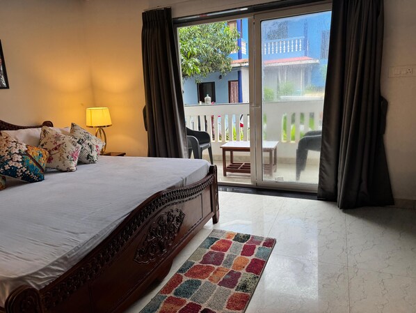 Camera d'albergo con un letto grande, un tavolino, una sedia, una lampada e vista sul balcone esterno.