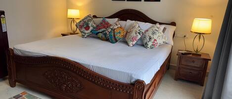 A neatly made bed with floral pillows, a wooden headboard, and a colorful rug. There are two bedside tables with lamps, and artwork on the wall.