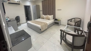 A modern hotel room with a bed, bedside table, desk, chairs, and an air conditioning unit. - HOTEL THE SAFFRON PARK (Panchkula)