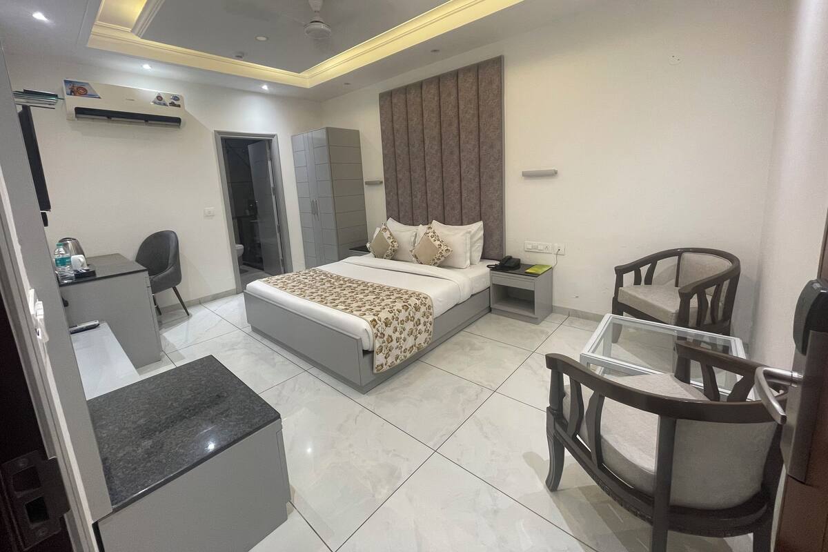 A modern hotel room with a bed, bedside table, desk, chairs, and an air conditioning unit.