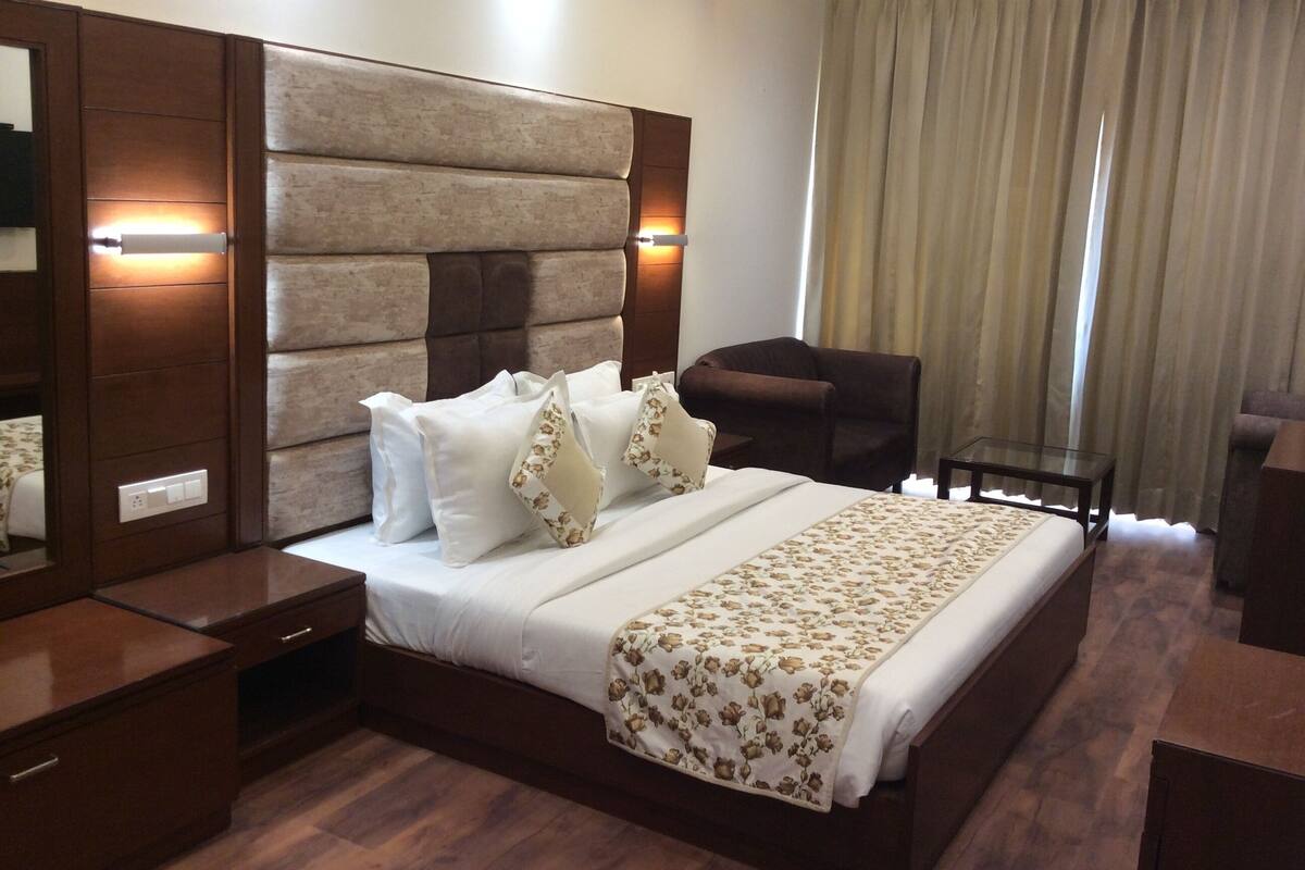 A hotel room with a large bed, a wooden headboard, two bedside tables, a chair, and a small table.