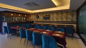 A restaurant with blue chairs and tables, a bar area, and a patterned wall. - HOTEL THE SAFFRON PARK (Panchkula)