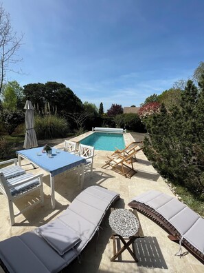 A poolside area with a table, chairs, lounge chairs, and a covered umbrella.