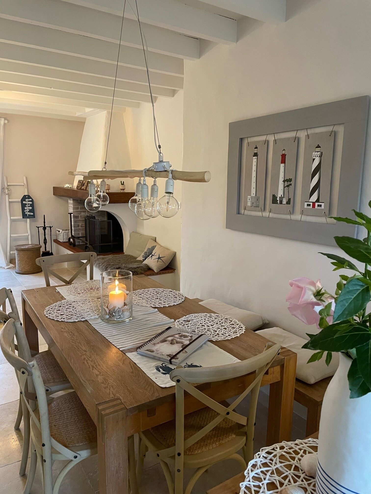 A dining area with a wooden table, white chairs, a candle, and a wall-mounted picture of lighthouses.