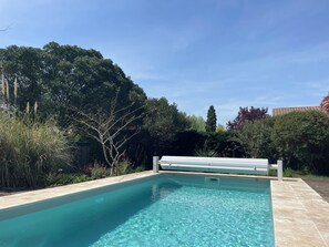 A clear swimming pool with a tiled edge, surrounded by lush greenery and trees.