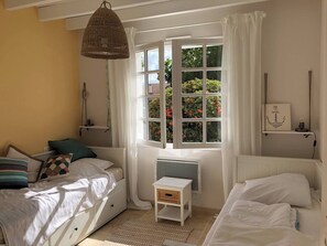 A bedroom with two beds, a window with curtains, a hanging light fixture, and a small bedside table.