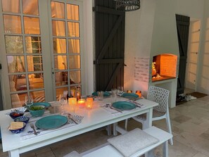 A dining table set with plates, glasses, and candles, surrounded by windows and a brick fireplace.