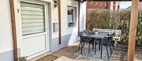 A covered patio with a table and chairs, a door, and a small potted plant.