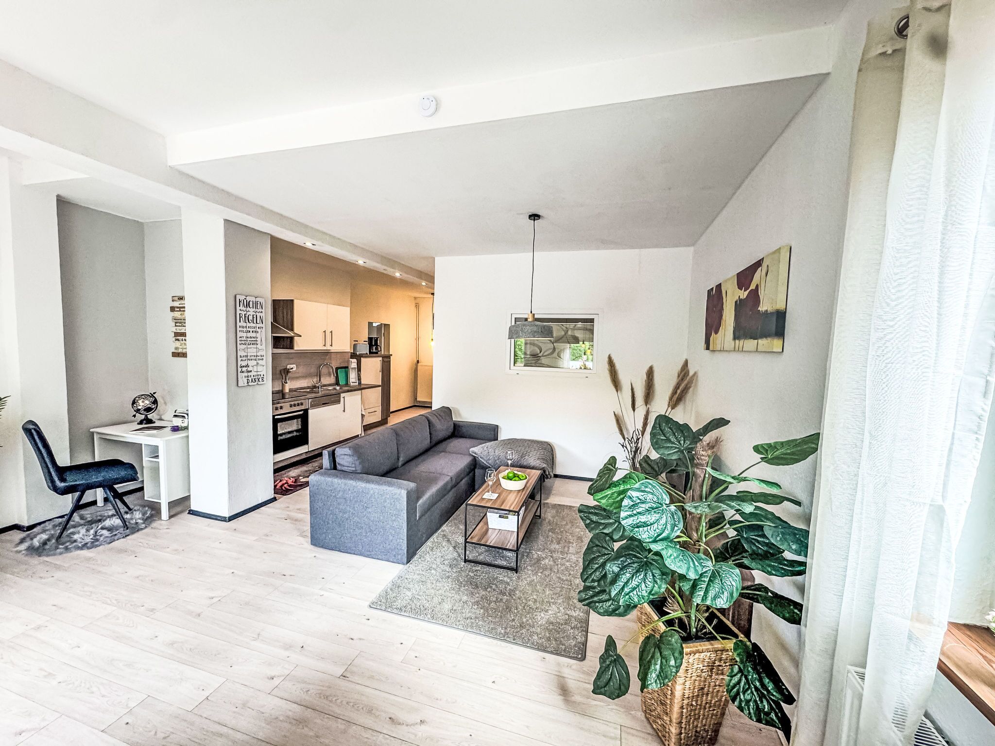 A modern living room with a grey sofa, a coffee table, and a dining area with a kitchen in the background.