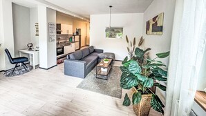 En moderne stue med en grå sofa, et sofabord og et spiseområde med et køkken i baggrunden.