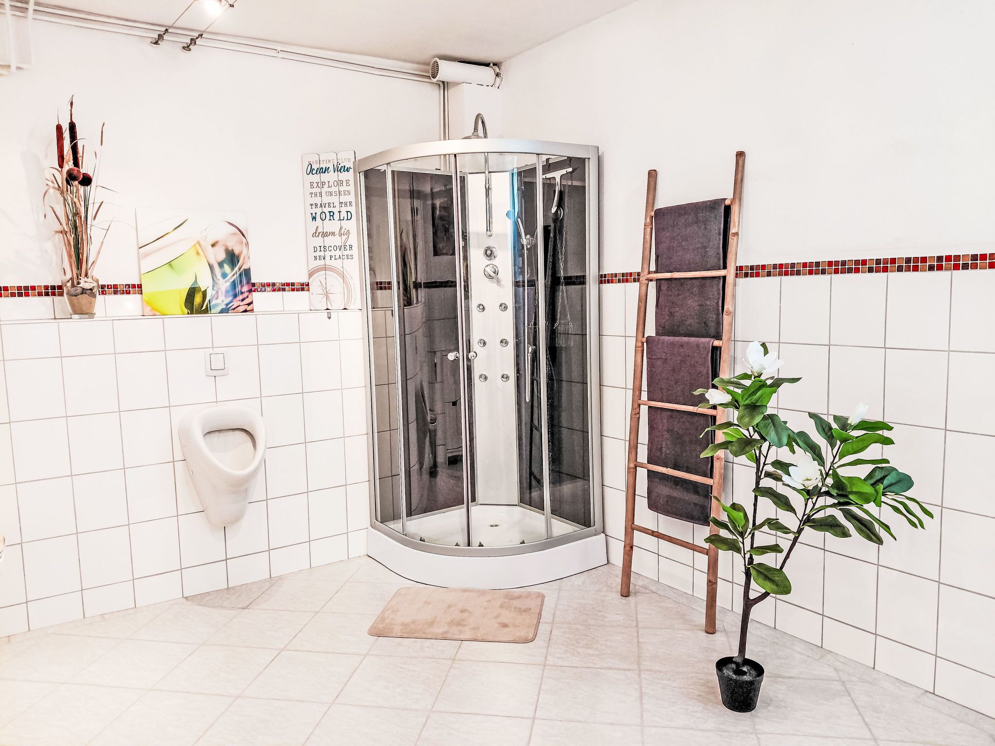 A corner bathroom with a glass-enclosed shower, a urinal, a towel rack, and a potted plant.