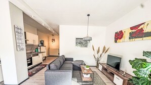 En moderne stue med en grå sofa, et sofabord, et TV-møbel og en stor plante.