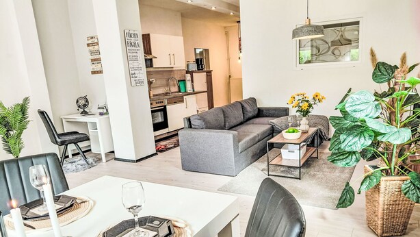 En moderne stue med en grå sofa, et spisebord med stearinlys og en stor grøn plante.