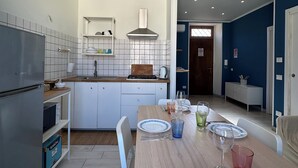A modern kitchen with white cabinets, a wooden countertop, and a dining table set with plates, glasses, and cutlery. - BlueBay Holiday Home (Torre del Greco)