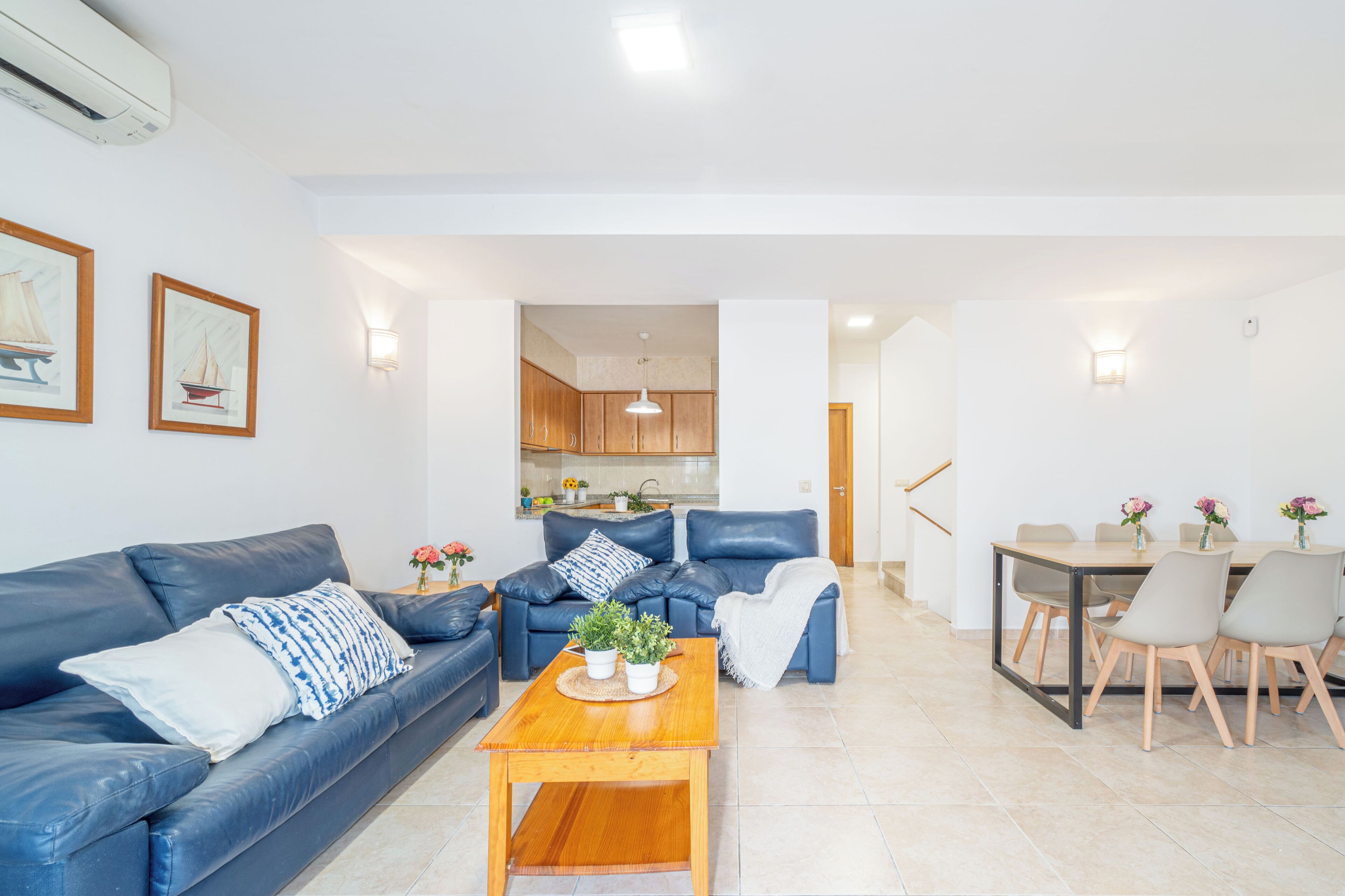 A modern living room with a blue sofa, a wooden coffee table, and a dining area with a table and chairs.