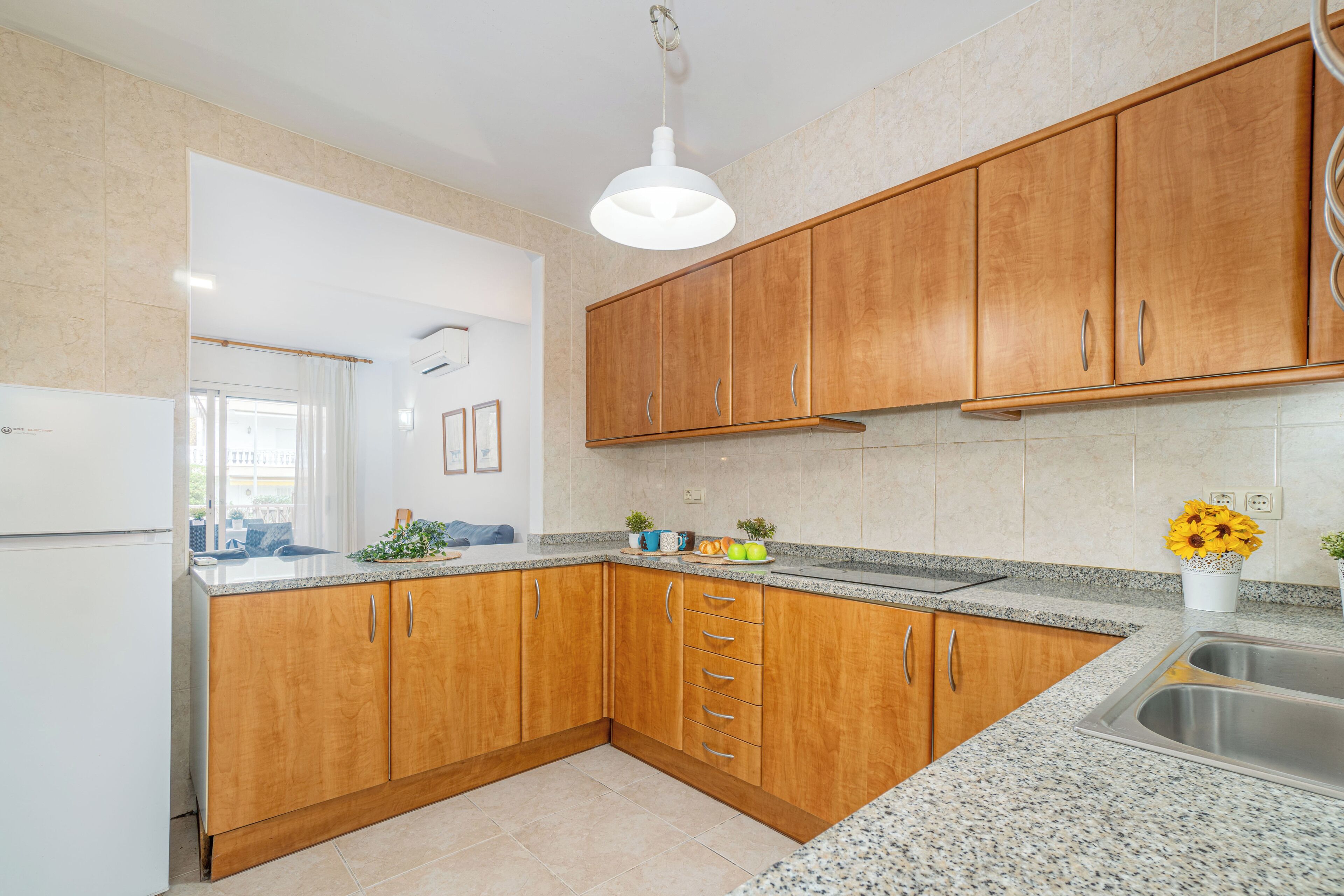 A kitchen with wooden cabinets, granite countertops, a stainless steel sink, and a ceiling light fixture.