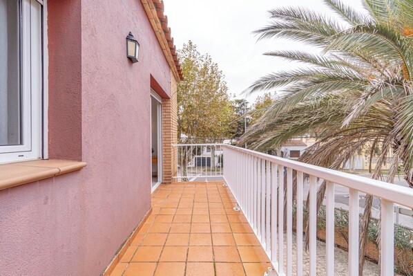 Een balkon met betegelde vloer, een witte reling en een roze gevel.