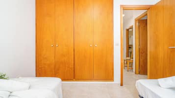 A bedroom with a large wooden wardrobe, a bed with white bedding, and a small table with a chair.