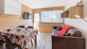 A cozy room with a wooden interior, a dining table with chairs, a sofa, and a TV mounted on the wall. - Les Asters by Interhome (Les Menuires)