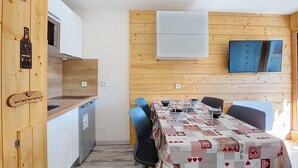 A compact kitchen with wooden cabinets and a dining area with a checkered tablecloth. - Les Asters by Interhome (Les Menuires)