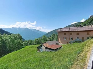 A hillside with a large building, a smaller structure, and mountains in the background.