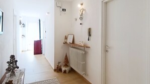 Un couloir avec un radiateur, une porte et une étagère sur laquelle est posé un panneau indiquant « Accueil ».