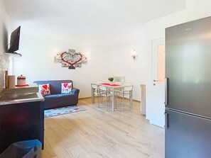 A compact living space with a kitchenette, a dining area, and a sofa with heart-themed cushions.
