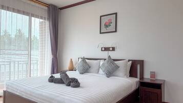 A neatly made bed with a striped white and gray duvet, a wooden nightstand with a vase, and a framed picture of flowers on the wall.
