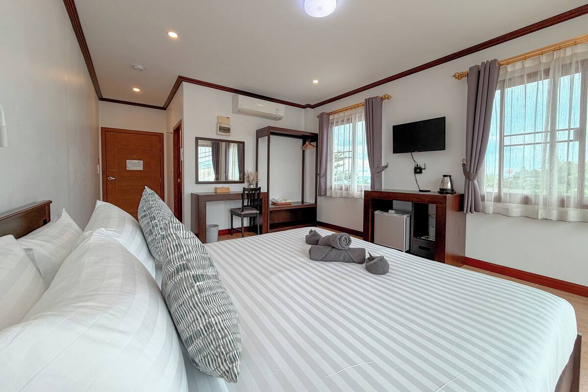 A hotel room with a large bed, a desk with a chair, a TV, and a window with curtains.