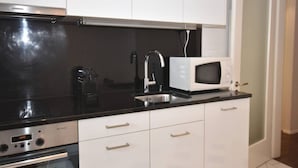 A compact kitchen with a microwave, sink, and stainless steel oven. - Charming studio near lake - Flower 42 (Zürich)