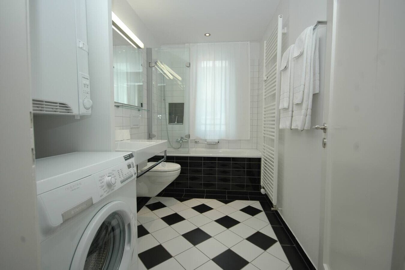 A compact bathroom with a washing machine, a toilet, and a bathtub.