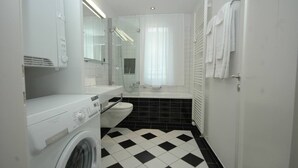 A compact bathroom with a washing machine, a toilet, and a bathtub. - Charming studio near lake - Flower 42 (Zürich)