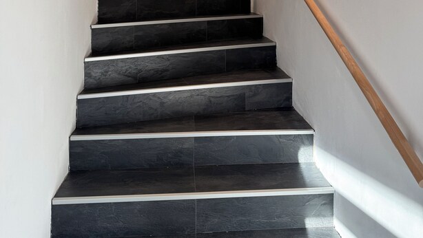 Eine moderne Treppe mit dunklen Steinstufen und Holzhandläufen, beleuchtet durch Wandleuchten.