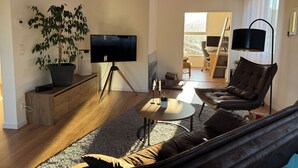 Ein modernes Wohnzimmer mit einem großen Flachbildfernseher, einer Zimmerpflanze, einem Sofa und einem Couchtisch.
