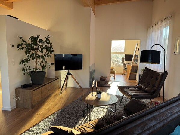 A modern living room with a large flat-screen TV, a potted plant, a sofa, and a coffee table.