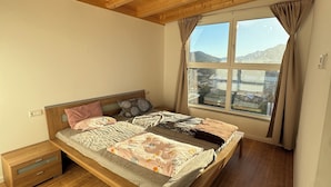 Ein Schlafzimmer mit einem Holzbett, einem Nachttisch, einem Fenster mit Vorhängen und Blick auf Berge.