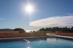 A swimming pool with clear blue water, surrounded by a low wall and a metal railing.