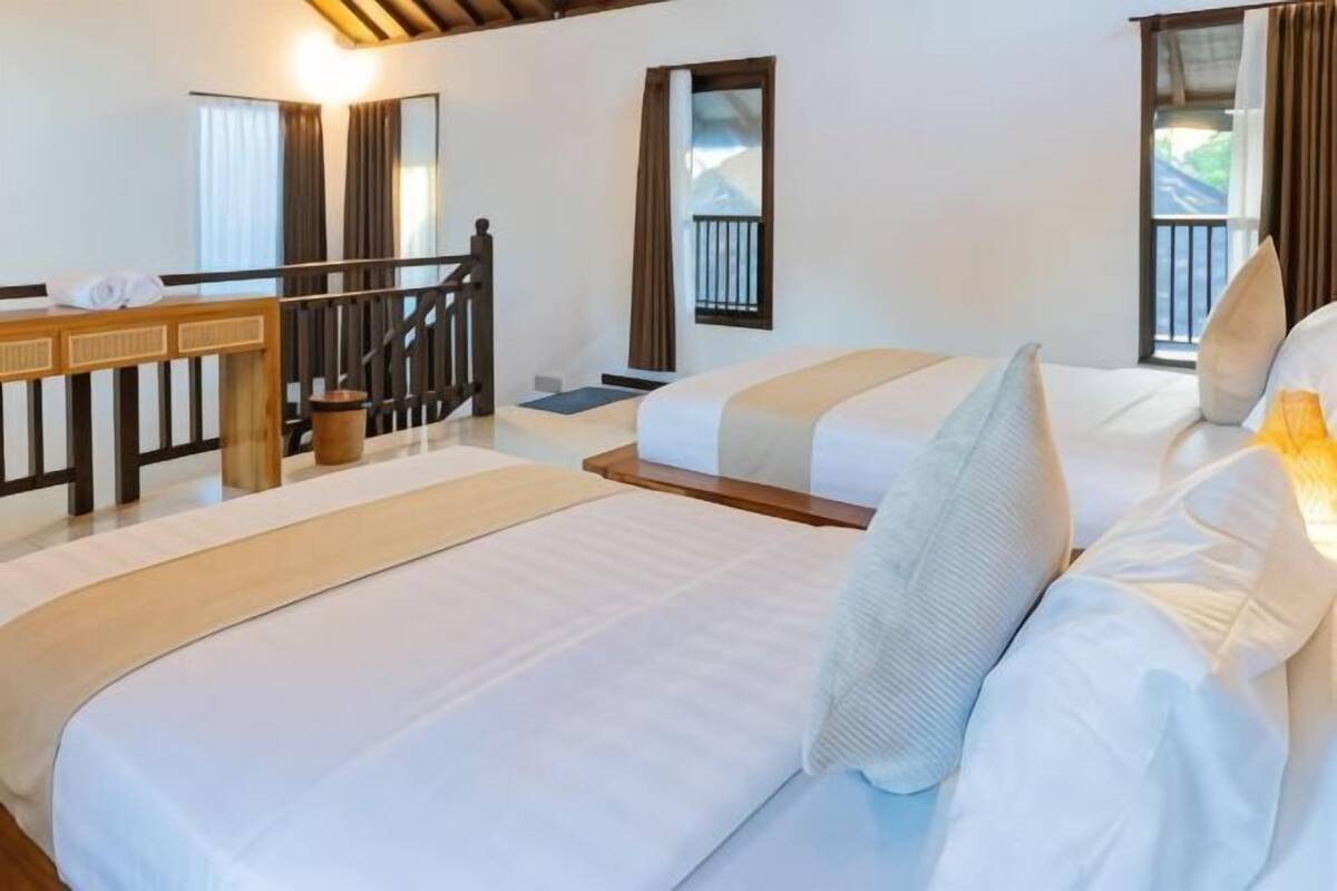 A hotel room with two beds, a wooden desk, and a balcony with a view of the mountains.