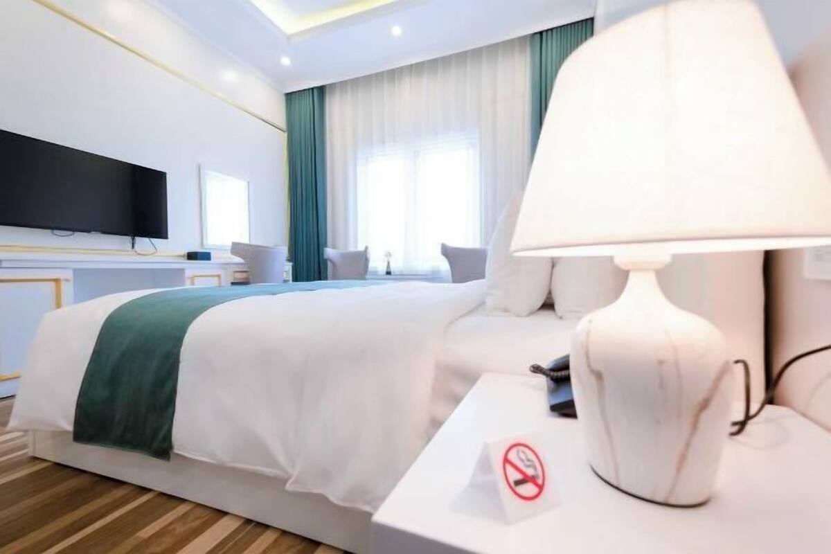 Habitación de hotel con cama, televisión, lámpara y cartel de prohibido fumar.