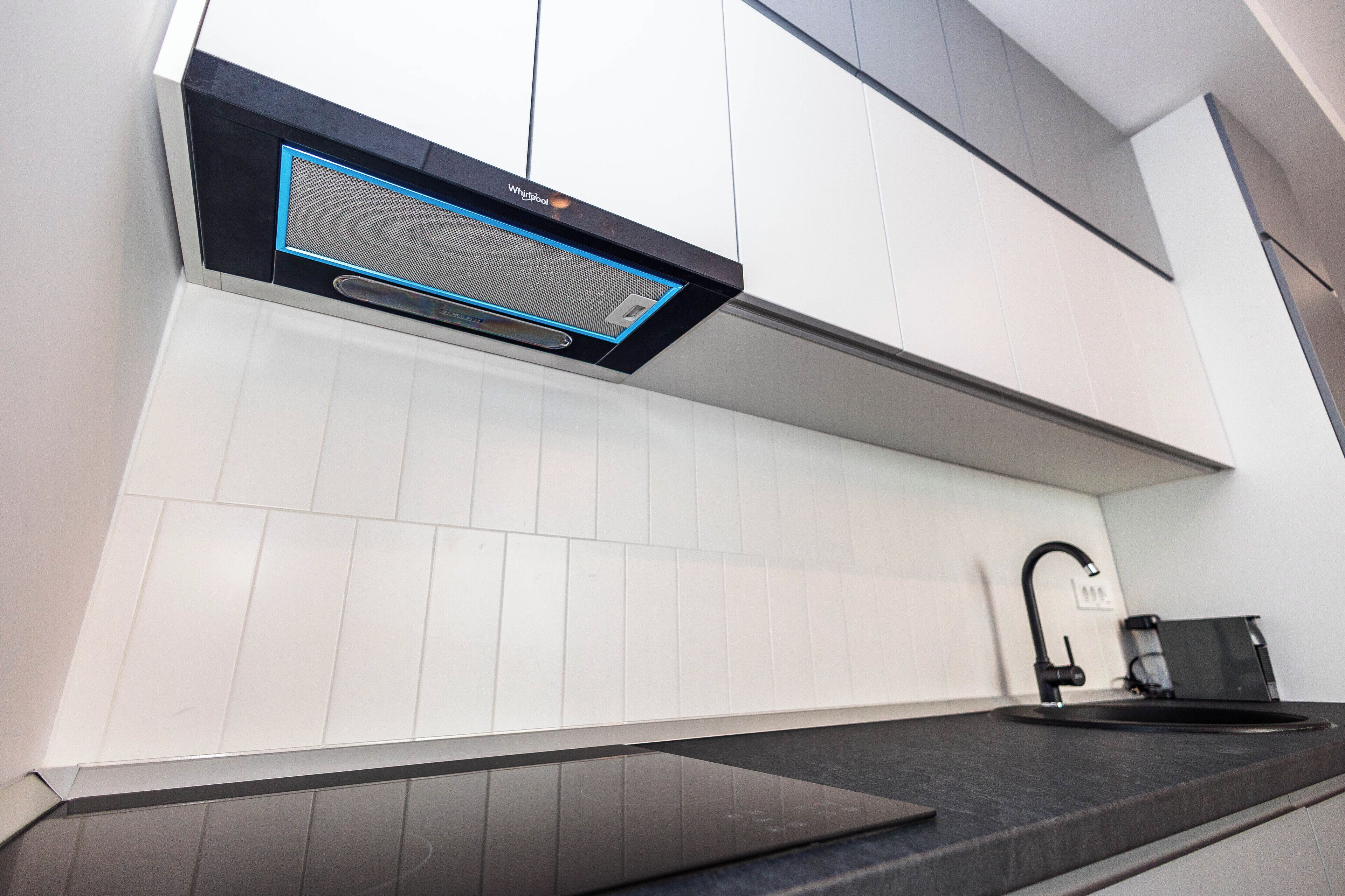 A modern kitchen with white cabinets, a black countertop, and a built-in range hood.