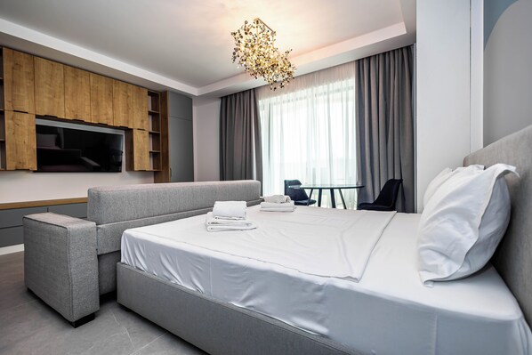 A modern hotel room with a large bed, a sofa, a TV mounted on the wall, and a dining area with a table and chairs. - Sol Axxis Nova (Navodari)