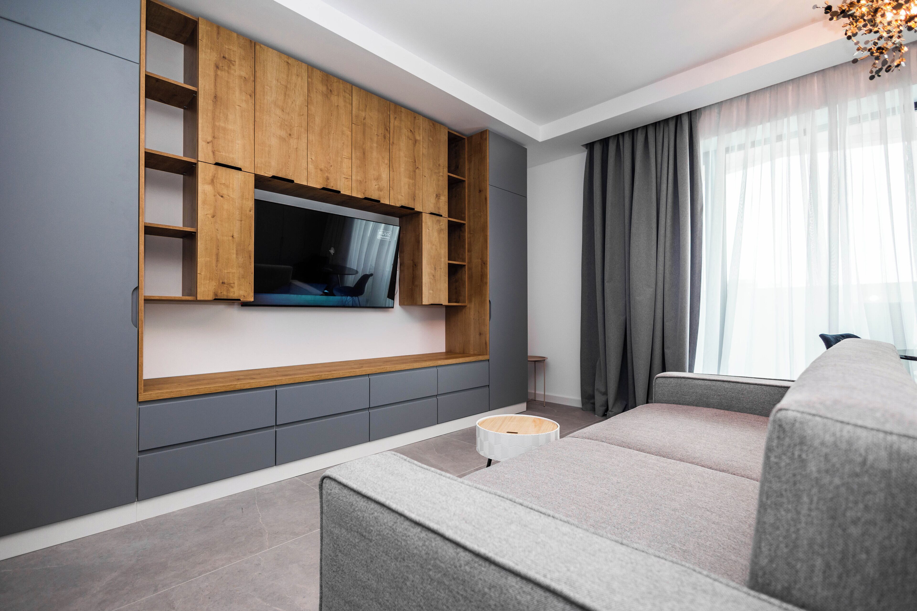 A modern living room with a built-in TV, grey sofa, and wooden shelving.