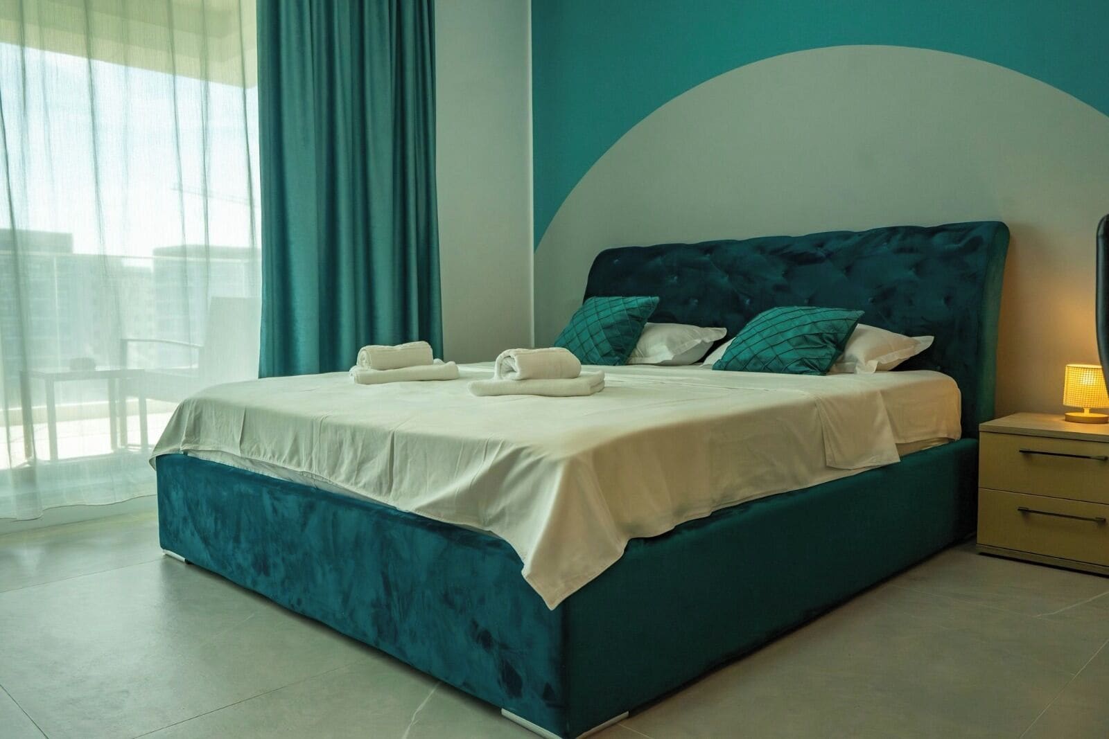 A modern bedroom with a large bed, a nightstand, and a view of the outdoors.