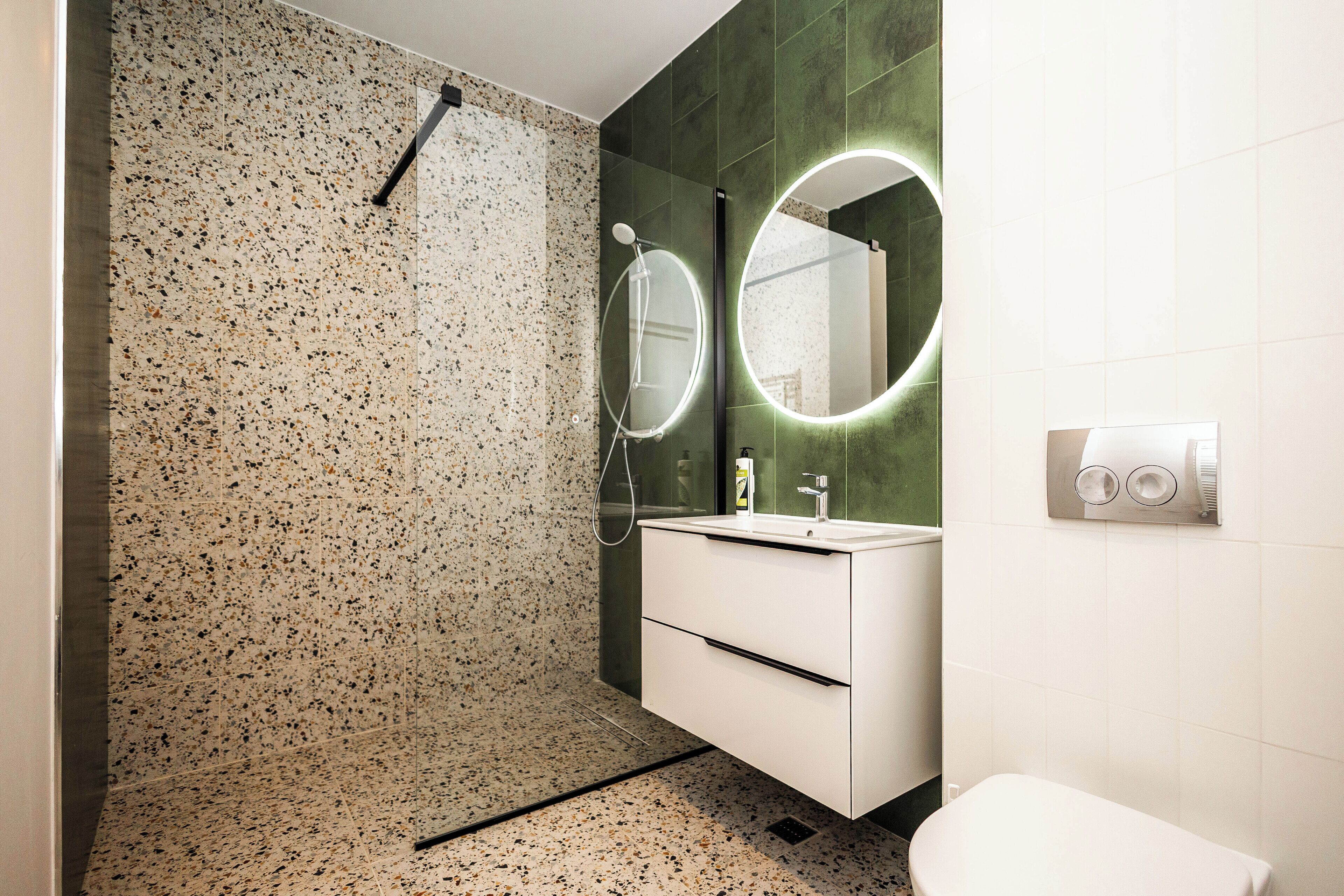 A modern bathroom with a speckled tile wall, a white vanity with a mirror, and a shower with a handheld showerhead.