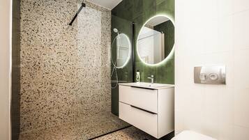 A modern bathroom with a speckled tile wall, a white vanity with a mirror, and a shower with a handheld showerhead.