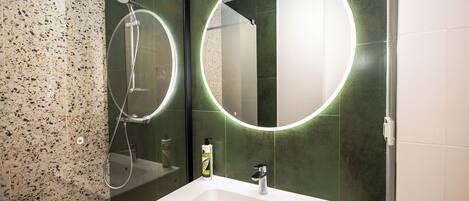 A bathroom with a white sink, a mirror with a circular light, and a shower area.