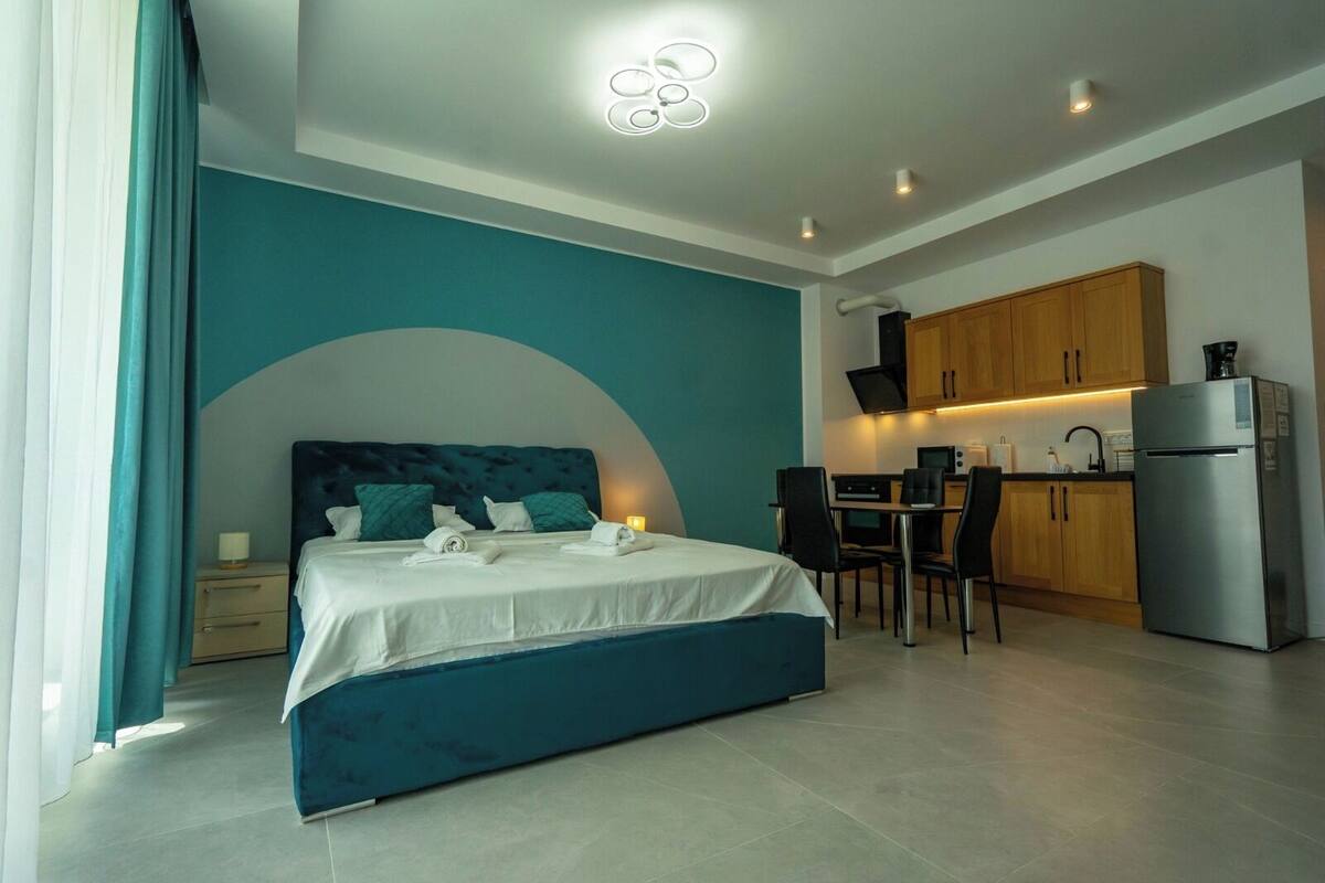 A modern hotel room with a bed, a desk, and a kitchenette.