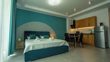 A modern hotel room with a bed, a desk, and a kitchenette.