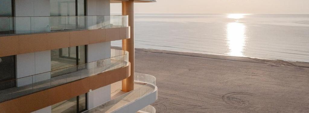 Un bâtiment moderne doté d’un balcon en verre donnant sur une plage.